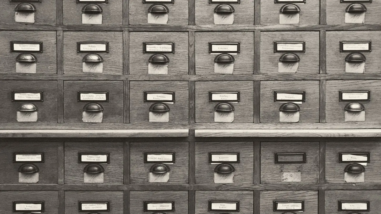 Black and white photo of a wooden library card catalogue with rows of labelled drawers and metal handles